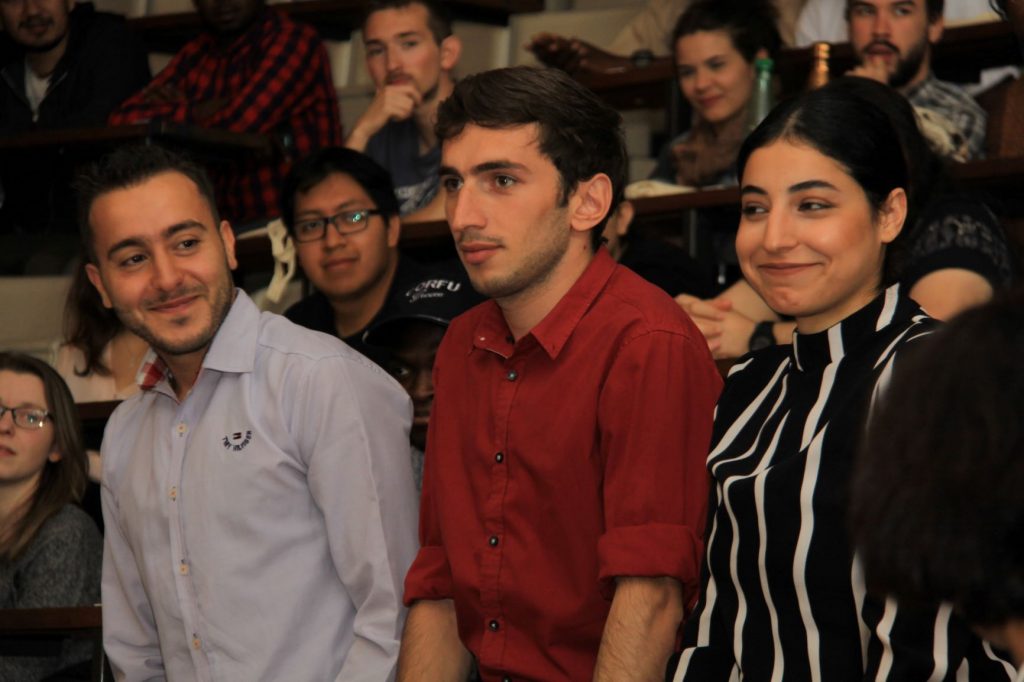 Deux jeunes hommes et une jeune femme souriants debout dans un amphi